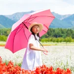 ピンクの傘を差して花畑を歩く9歳の娘